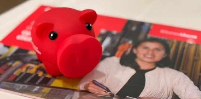 Alcancía roja sobre revista institucional, símbolo de ahorro y fortalecimiento del emprendimiento.